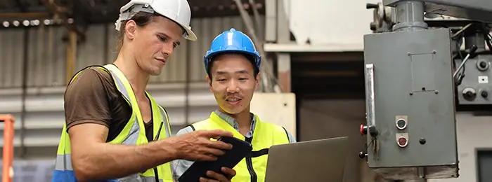 Technician in protective uniform with hardhat standing and teaching colleague worker to use computerized machine control at heavy industry manufacturing factory|AdobeStock#555021484